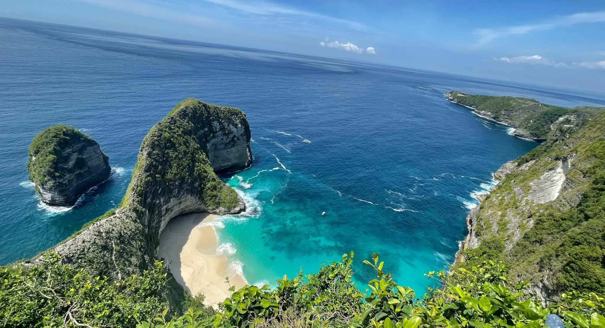 Kelingking Beach on Nusa Penida seen from the clifftop — a green headland shaped like a T-Rex dropping to white sand and turquoise sea